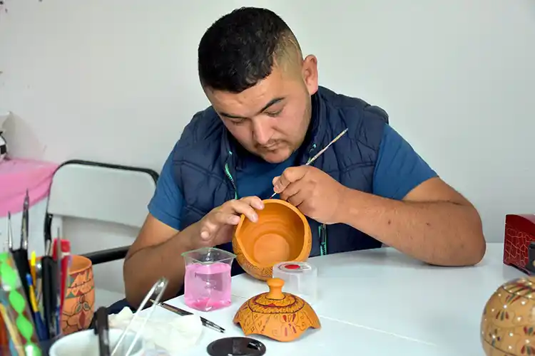 Bir katılımcı atölye masasında ince fırça işçiliğiyle geleneksel motifli bir eser boyuyor.